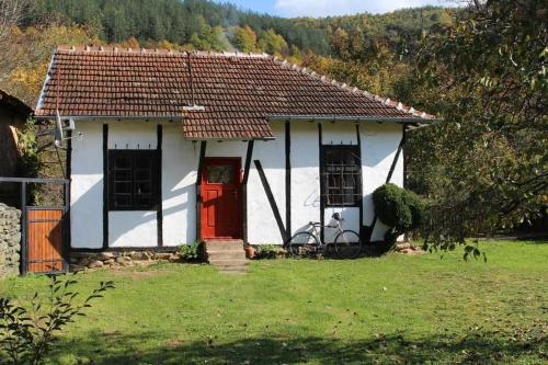 uma pequena casa branca com uma porta vermelha em Глинената къща в Дълги Дел em Dŭlgi Del