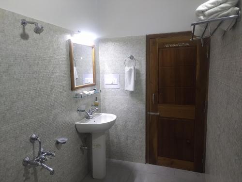 baño con lavabo, espejo y puerta en The Camellia en Dibrugarh