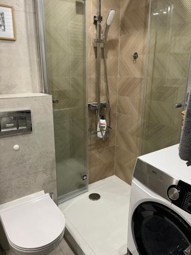 a bathroom with a shower with a toilet and a washing machine at Apartament Akademicka in Białystok