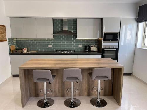 a kitchen with a wooden island with three bar stools at Sunset Apt Modern 1 bedroom Apt near the Beach in Birżebbuġa