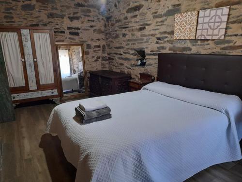 ein Schlafzimmer mit einem weißen Bett und einer Steinmauer in der Unterkunft Casiña do Cereixeiro Roblido in Roblido