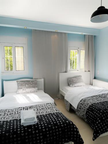 Kallikratis Apartment Near Athens Airport في سباتا: سريرين في غرفة مع جدران ونوافذ زرقاء