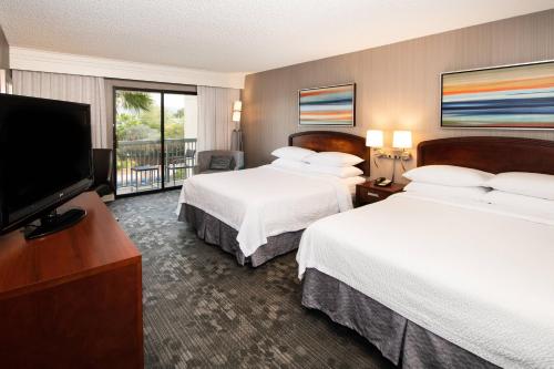 a hotel room with two beds and a flat screen tv at Courtyard by Marriott Oakland Airport in Oakland