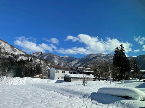 a snow covered field with a house in the mountains at GuestHouse Shirakawa-Go INN in Shirakawa