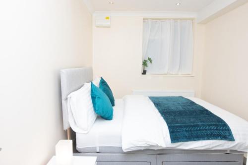 a white bedroom with a bed with blue pillows at Evergreen Apartments-Flat 7, London in London