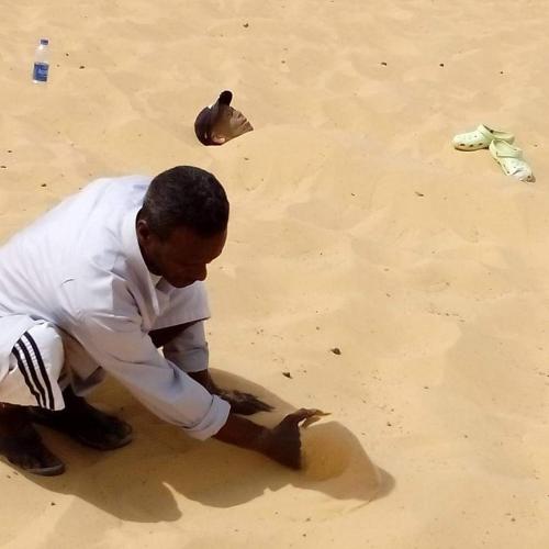 a man kneeling on the ground in the sand at Kayan Guest House in Aswan