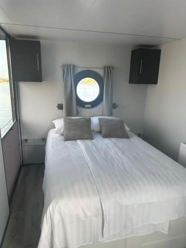 een groot wit bed in een kleine kamer met een raam bij Stoere HOUSEBOAT op toplocatie! in Belt-Schutsloot