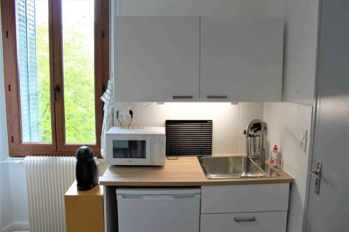 une cuisine avec des armoires blanches, un évier et un micro-ondes dans l'établissement Très beau studio centre ville, au calme, à Annecy