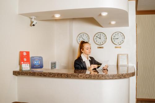 a woman sitting at a counter with clocks on the wall at Non-stop hotel in Boryspilʼ