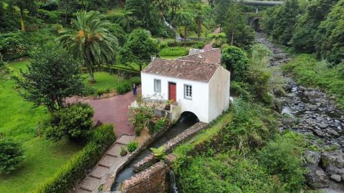 a small white house with a red door next to a river at Ribeira do Guilherme - Watermill house Botanic Garden in Nordeste