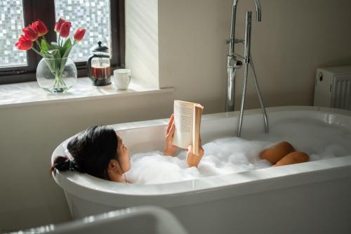 une femme qui se couche dans une baignoire en lisant un livre dans l'établissement The Manor, à Little Dean