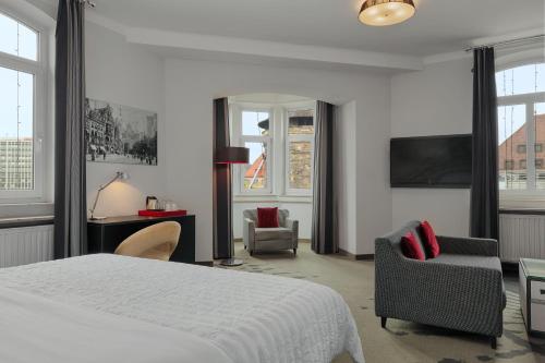 a bedroom with a bed and two chairs and a tv at Le Méridien Grand Hotel Nürnberg in Nuremberg
