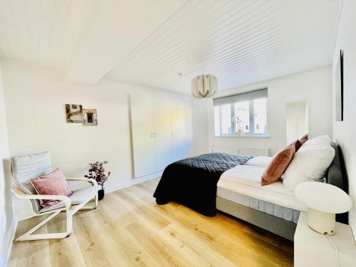 um quarto branco com uma cama e uma cadeira em aday - Charming apartment in the pedestrian street of Frederikshavn em Frederikshavn