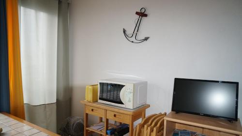 une télévision et un micro-ondes sur une table avec une télévision dans l'établissement Ancre et Mouettes, à Saint-Cyprien
