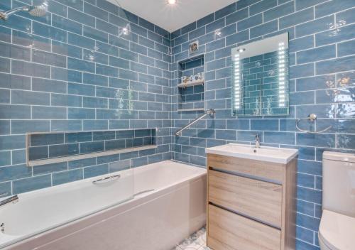 a blue tiled bathroom with a tub and a sink at Gorwel in Abersoch