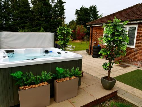 a hot tub in a garden with two potted trees at Deluxe 4 5 Bed Hot Tub Cinema Room 15 in Saffron Walden