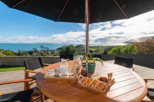 a wooden table with a basket of bread and an umbrella at Luxury Lookout - Cable Bay Holiday Home in Cable Bay