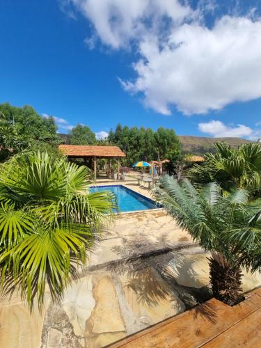 a swimming pool with palm trees and a gazebo at Chalés Encantos da Serra in Carrancas