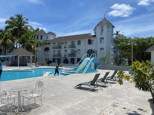 Ocho Rios Vacation Resort Property Rentals في أوتشو ريوس: مسبح بزحليقة وكراسي ومبنى