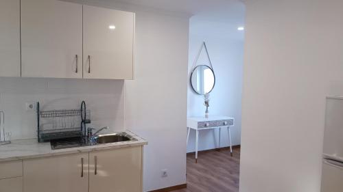 cocina con armarios blancos, lavabo y espejo en Mondalva Apartamentos, en São Pedro de Alva