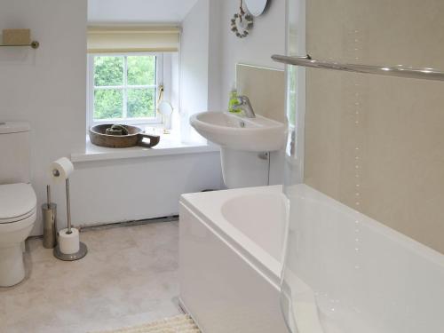 a white bathroom with a tub and a sink and a toilet at Wisteria Cottage in Alnham