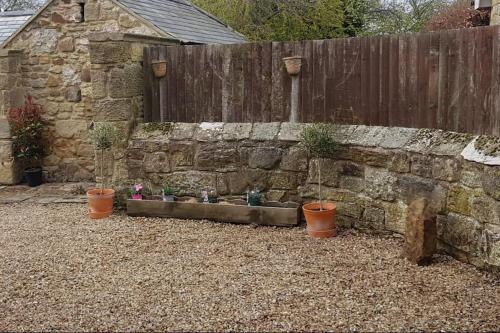 a stone wall with three potted plants next to a fence at Hare view Cottage - Northumberland 