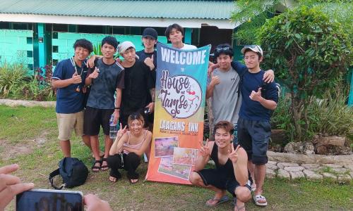 a group of people posing for a picture next to a sign at House of TamSe Laagans ' Inn in Badian