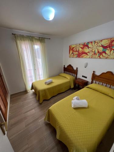 two beds in a room with yellow sheets at Casa Montse in Cala Galdana