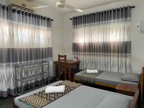 a room with two beds and curtains and a table at Berty's Cottage in Jaffna