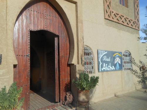 a building with a wooden door with a sign on it at Riad Aicha & Camel Trekking in Merzouga