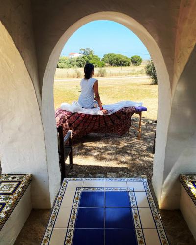 a woman sitting on a table looking out of a window at Casa Flor de Sal in Moncarapacho
