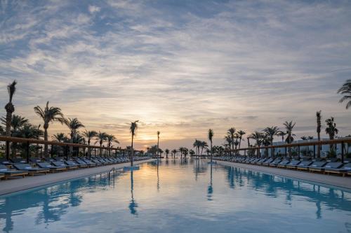 a pool with chairs and palm trees at sunset at Serry Beach Resort in Hurghada