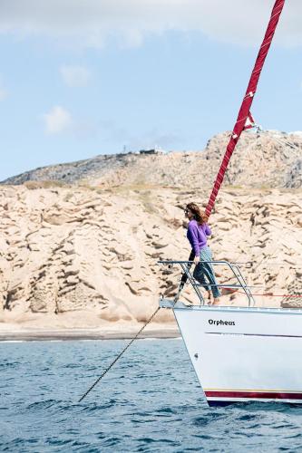 uma mulher na proa de um barco na água em Orpheus em Chora, Ios