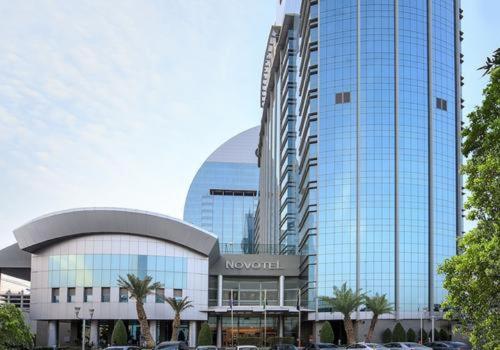 Novotel Riyadh Al Anoud في الرياض: مبنى زجاجي كبير فيه سيارات تقف امامه