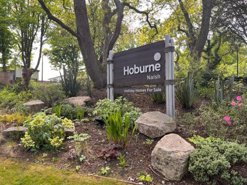 a sign in a garden with flowers and rocks at Home by the sea, Hoburne Naish Resort, sleeps 4, on site leisure complex available in Milford on Sea