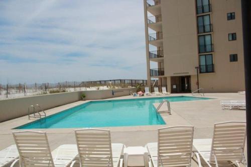 a swimming pool with white chairs and a building at Wind Drift 102S by ALBVR - 2BR, 2BA Beautiful Upgraded Beachfront Condo near Flora Bama, Outdoor Pools and Tennis Courts in Orange Beach