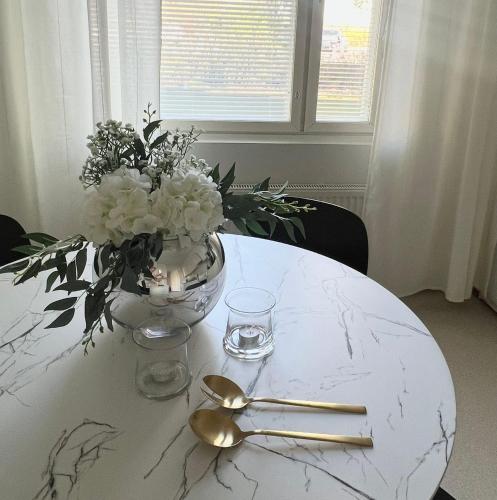 a white table with a vase of flowers and gold spoons at Annalan Helmi - Viihtyisä koti hyvillä kulkuyhteyksillä ja saunalla in Tampere