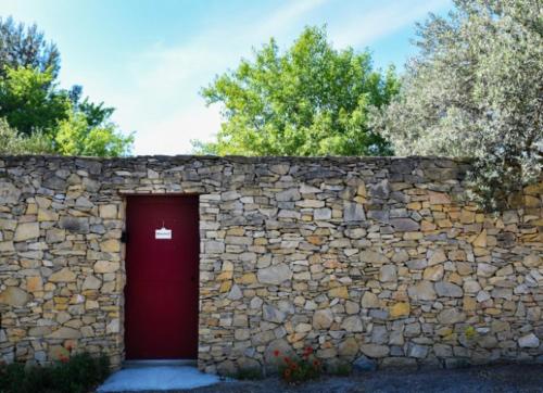 una pared de piedra con una puerta roja delante en Maison d'hotes - chambre-kitchenette-salle de bain-espace extèrieur, en Nimes