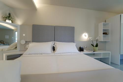 a white bedroom with a large bed and a desk at Hotel Village Eden in Capo Vaticano