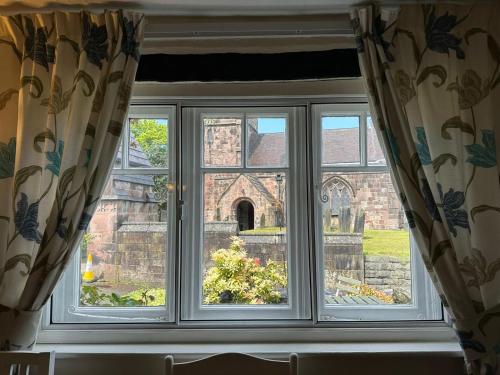 a window with curtains looking out at a church at Chapter Cottage, Cheddleton Nr Alton Towers, Peak District, Foxfield Barns in Cheddleton