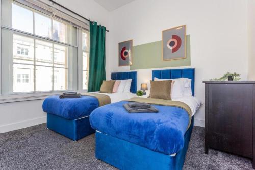 a bedroom with two beds with blue ottomans at Newcastle's Most Central Apartment - Sleeps 10 in Newcastle upon Tyne