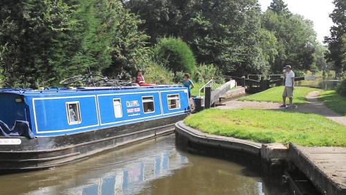 a blue boat on a river with people on it at Narrowboat canal holiday from19th august in Aldermaston