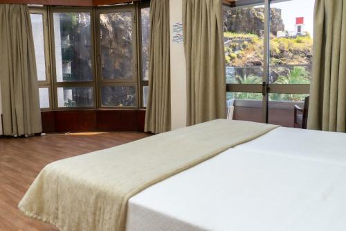 a bedroom with a white bed and large windows at Flag Hotel Madeira - Ribeira Brava in Ribeira Brava