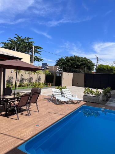 a swimming pool with chairs and a table and an umbrella at Casa de Temporada Mouton in Olímpia