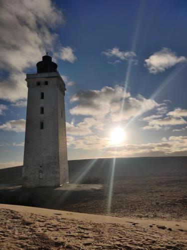 a lighthouse on the beach with the sun in the sky at Ferielejlighed Rubjerg Præstegård in Løkken
