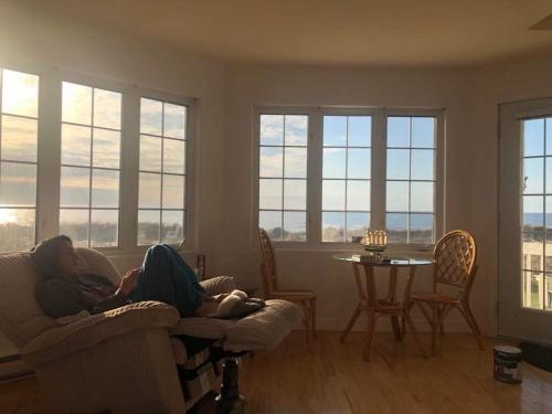Dos mujeres tumbadas en un sofá en una sala de estar con ventanas en Phare des Dunes Lighthouse, en Tracadie