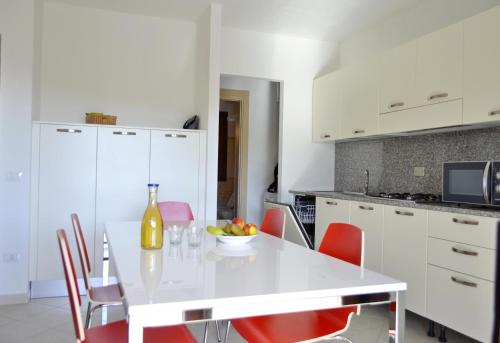 a white kitchen with a white table and red chairs at GF Apartments La Vigna in Badesi