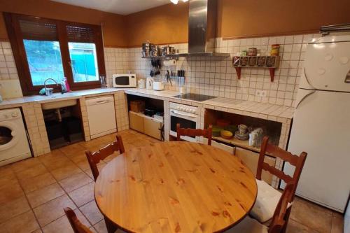 cocina con mesa de madera con sillas y nevera blanca en La casa del fresno, en Pinilla del Valle