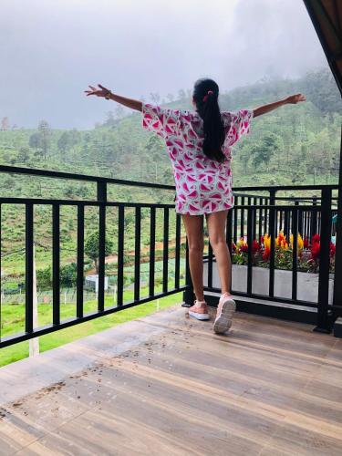 a woman in a dress standing on a balcony looking at a view at Queensland Hotel in Nuwara Eliya