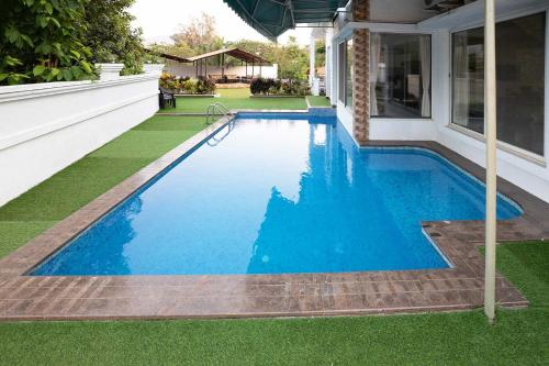 a swimming pool with blue water and green grass at Casa Serenity by StayVista - Relax with a pool, lawn, and inviting jacuzzi in Lonavala